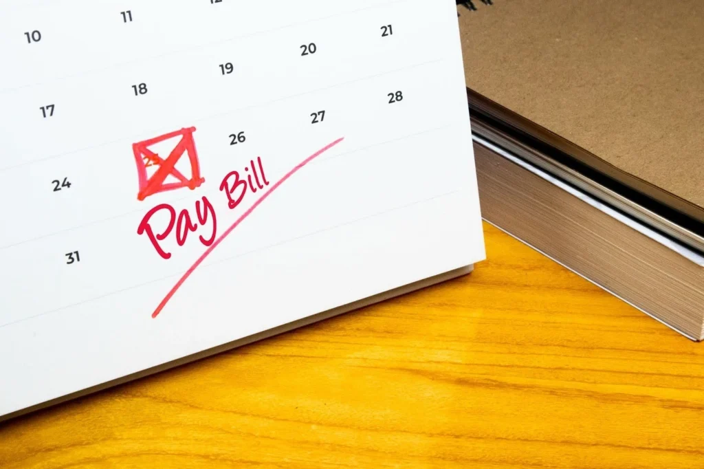 close up on calendar with cross on number 25 with handwritten and underlined "pay bill" in red ink