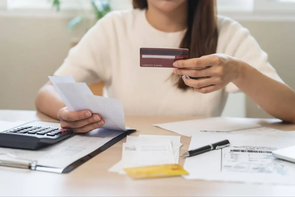 woman sitting at table with financial documents and receipts holding up credit card working to pay debts for her savings goals