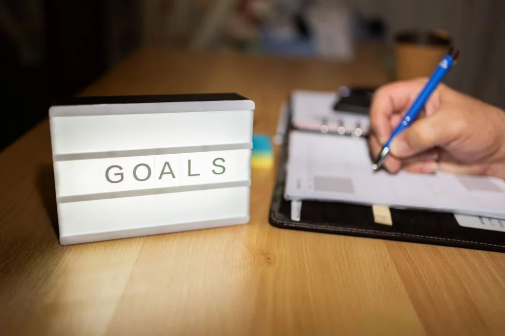 view of hand writing savings goals in diary next to light up sign saying "goals"