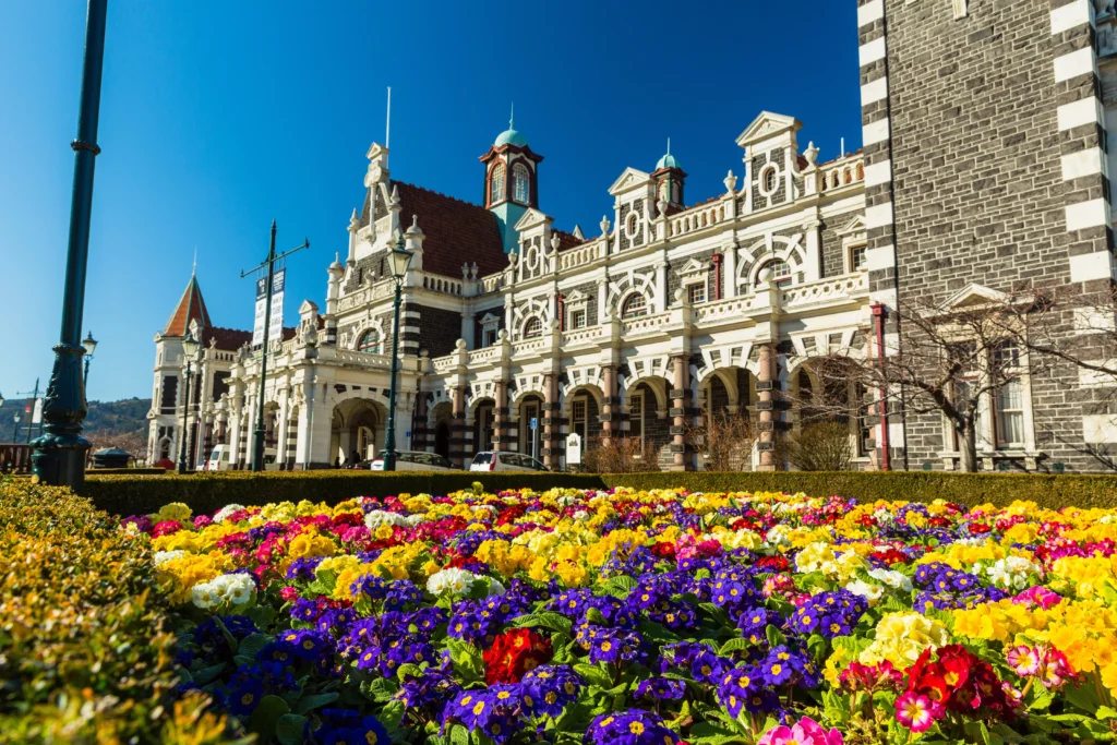 Intricate Victorian building in Dunedin New Zealand with huge flowerbed of various colours in front