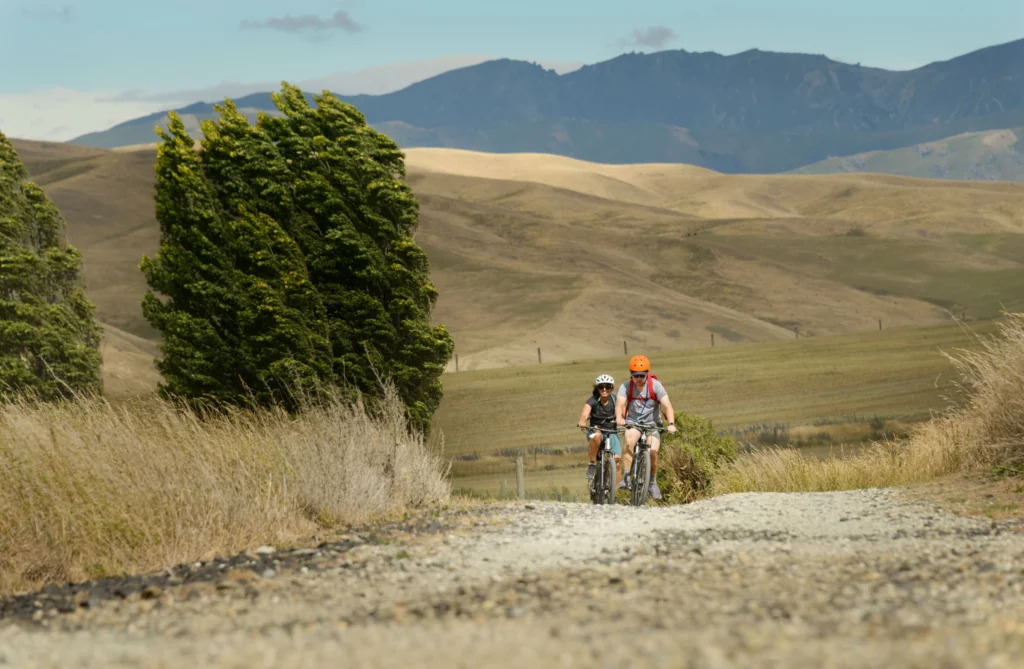 Two cyclists on dry, windy plains on the Otago Central Rail Trail in New Zealand