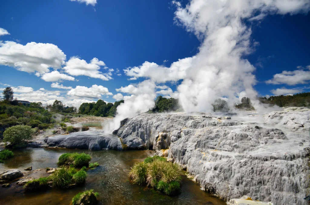 Active geyser with lots of white smoke on grey rocks by a mudpool in Rotorua New Zealand