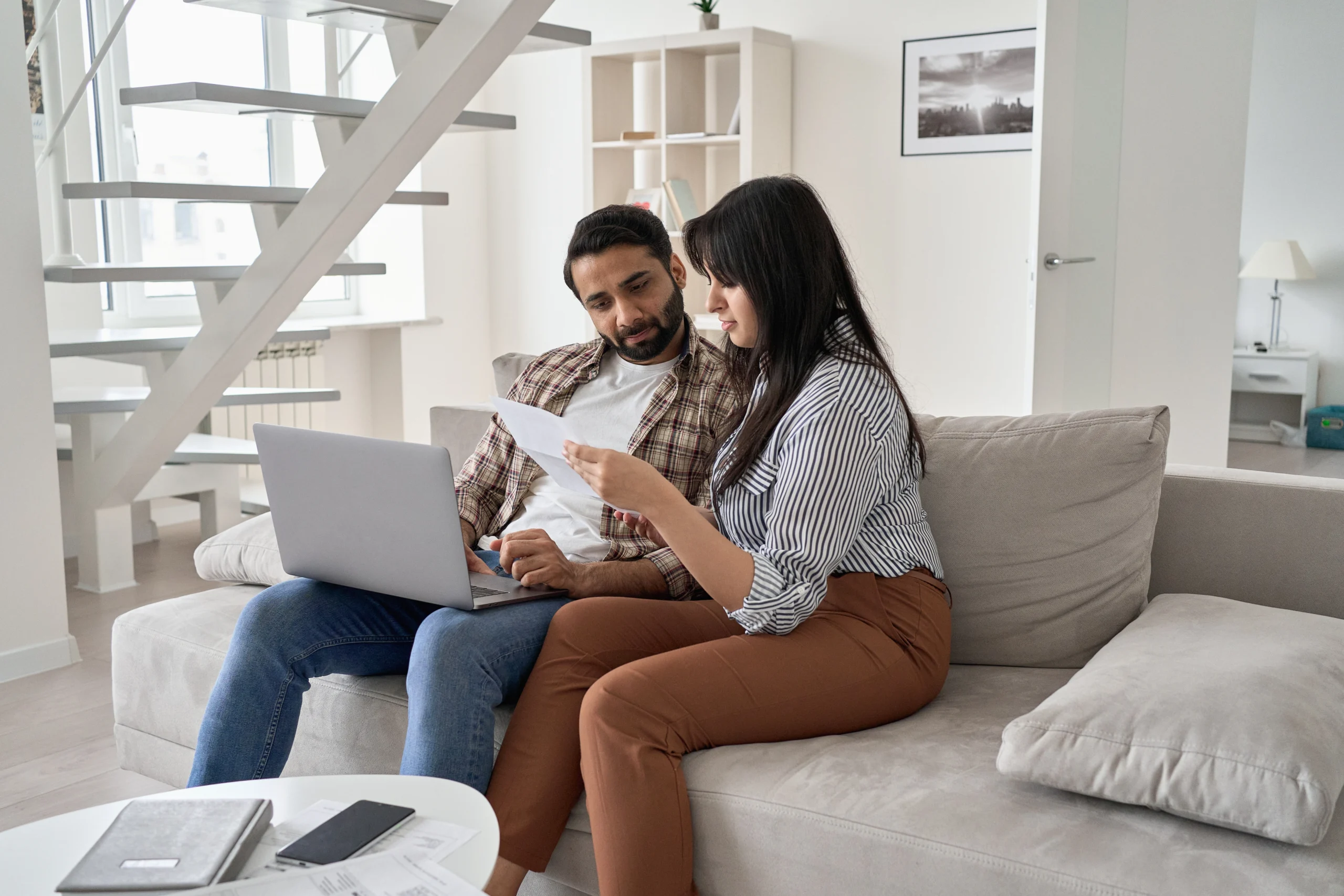 A couple looks over a bill while creating a budget on a beige couch