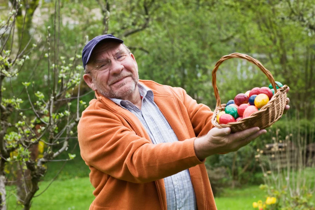 elderly man with soft smile holding up a woven basket full of coloured eggs after an Easter egg hunt