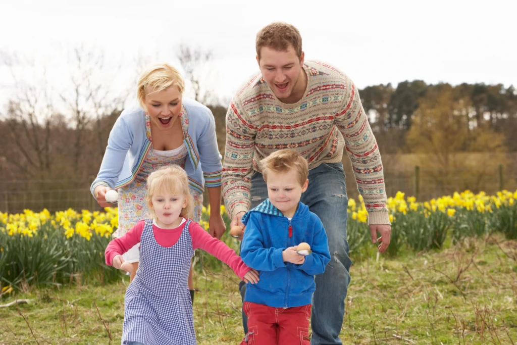 two parents and two kids holding an egg and spoon each excitedly racing in a garden