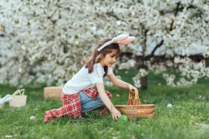 little girl with bunny ears holding a wicker basket picking up a green egg in the grass doing an Easter egg hunt