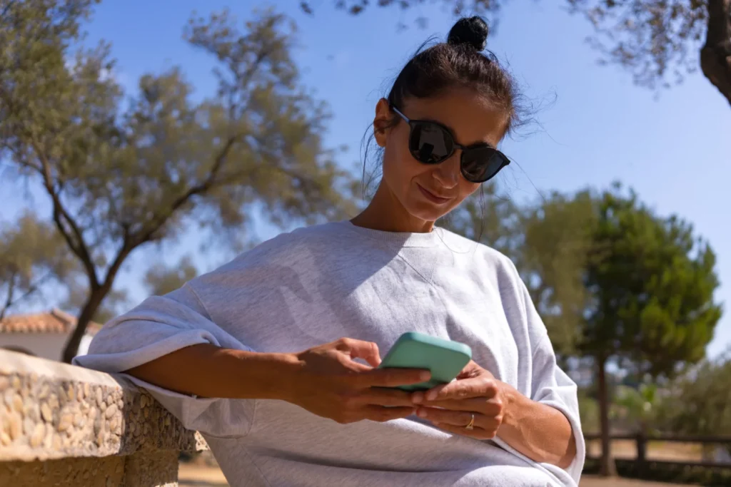 Woman leaning on short concrete pillar outside looking at her phone as she researches getting a loan fast with no credit