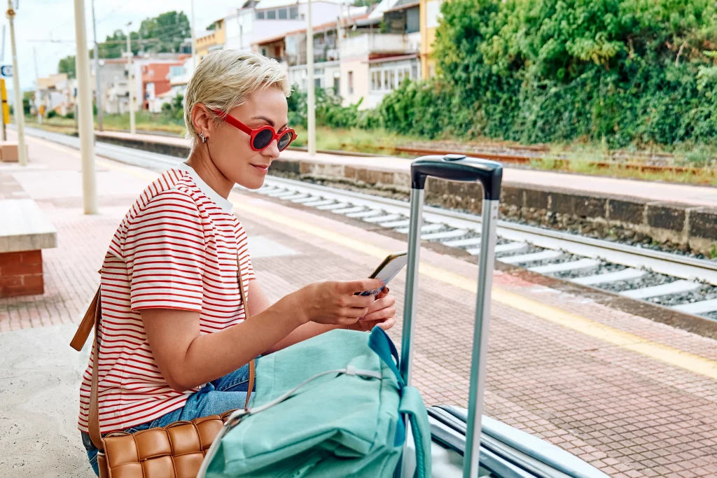Woman on her phone with suitcase and bags waiting at the train station as she applies for a same day loan with Swoosh Finance NZ