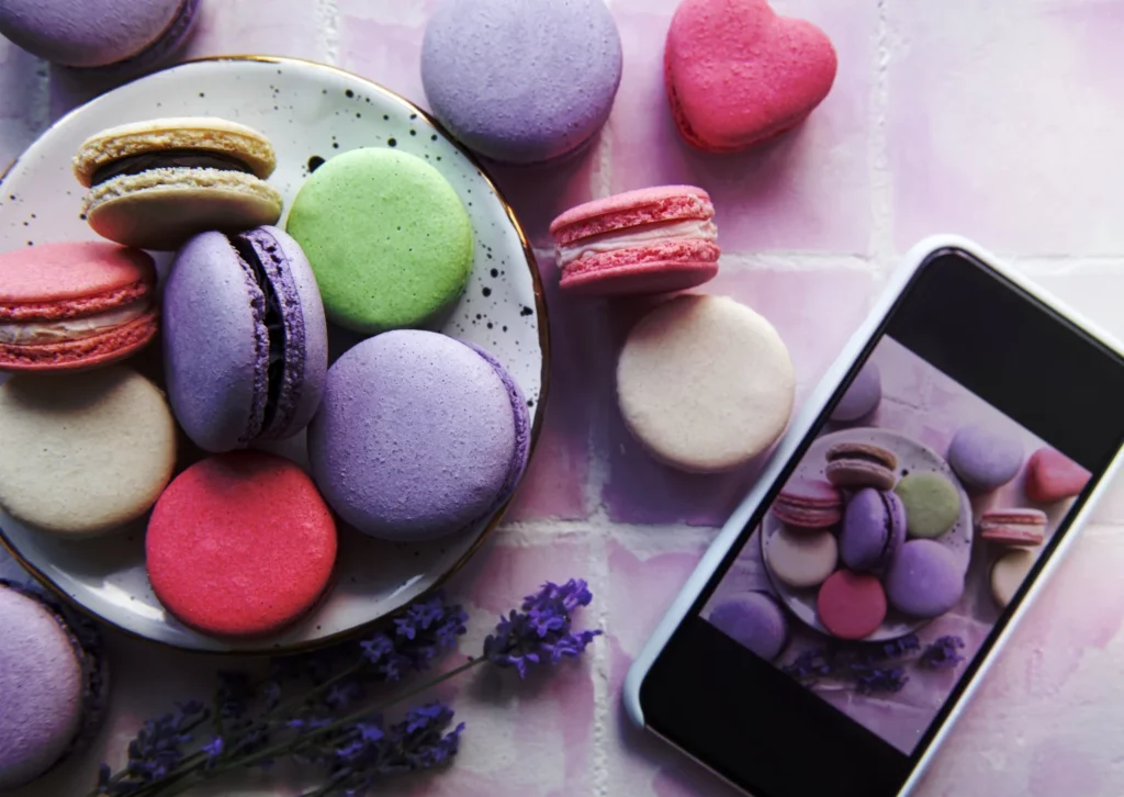 Plate of aesthetically pleasing macarons and lavender flowers next to phone showing photo of the plate