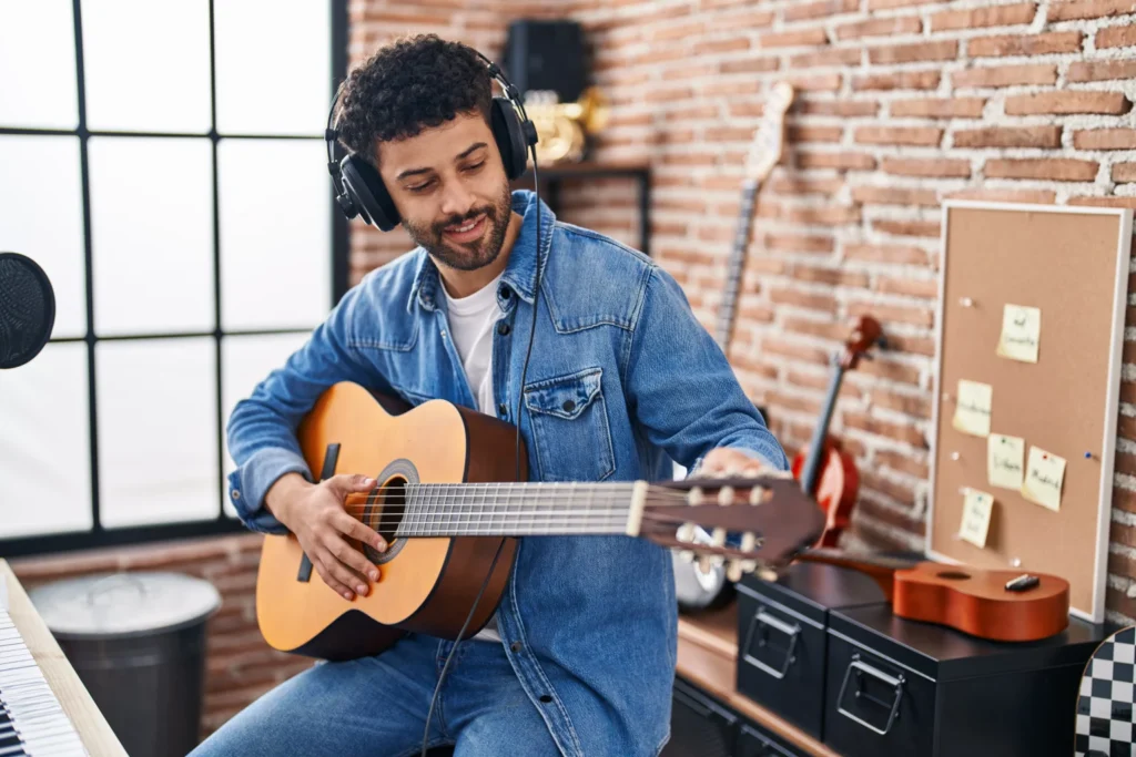 Man wearing headphones tuning his guitar in music room to record a song to make money online