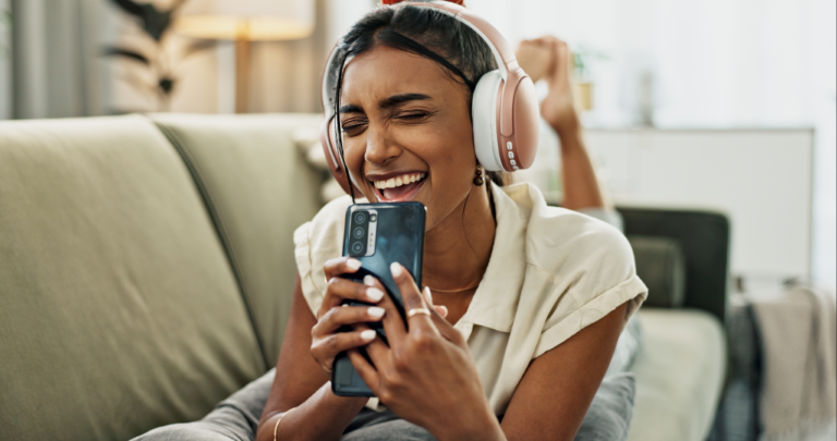 woman laying on her couch with headphones singing happily into her phone like it is a microphone because she got a quick loan