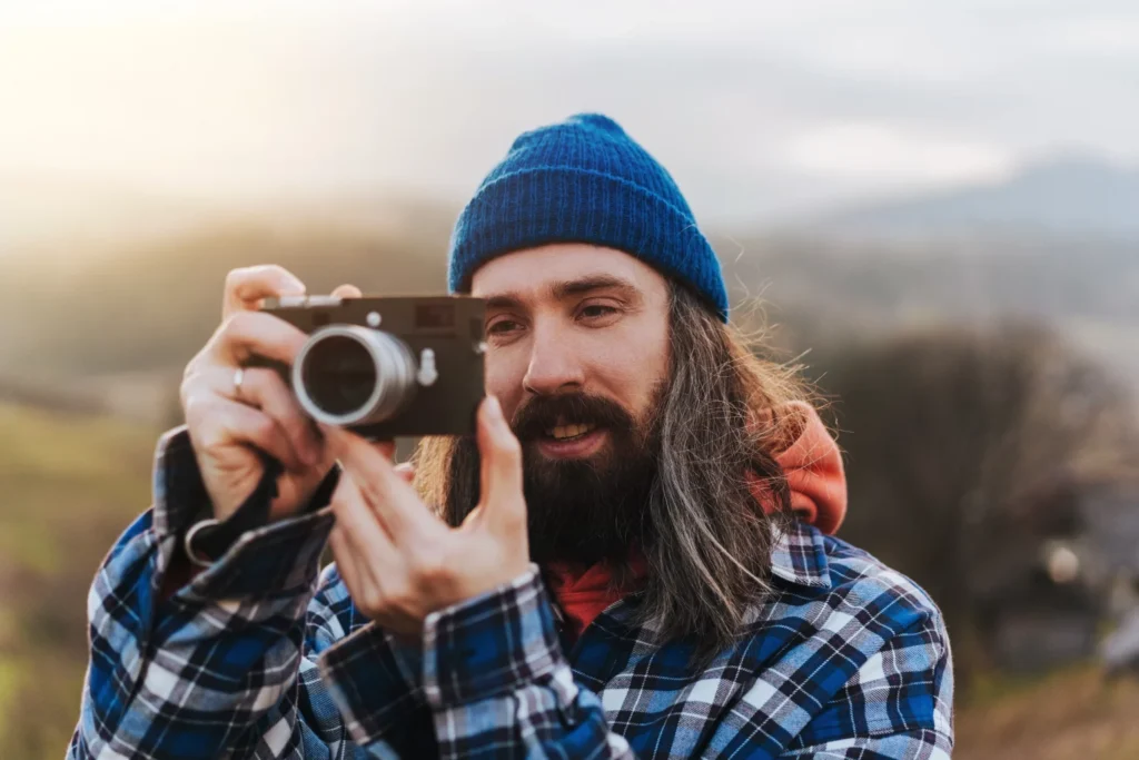 Man in beanie and hoodie outdoors taking photos with a digital camera