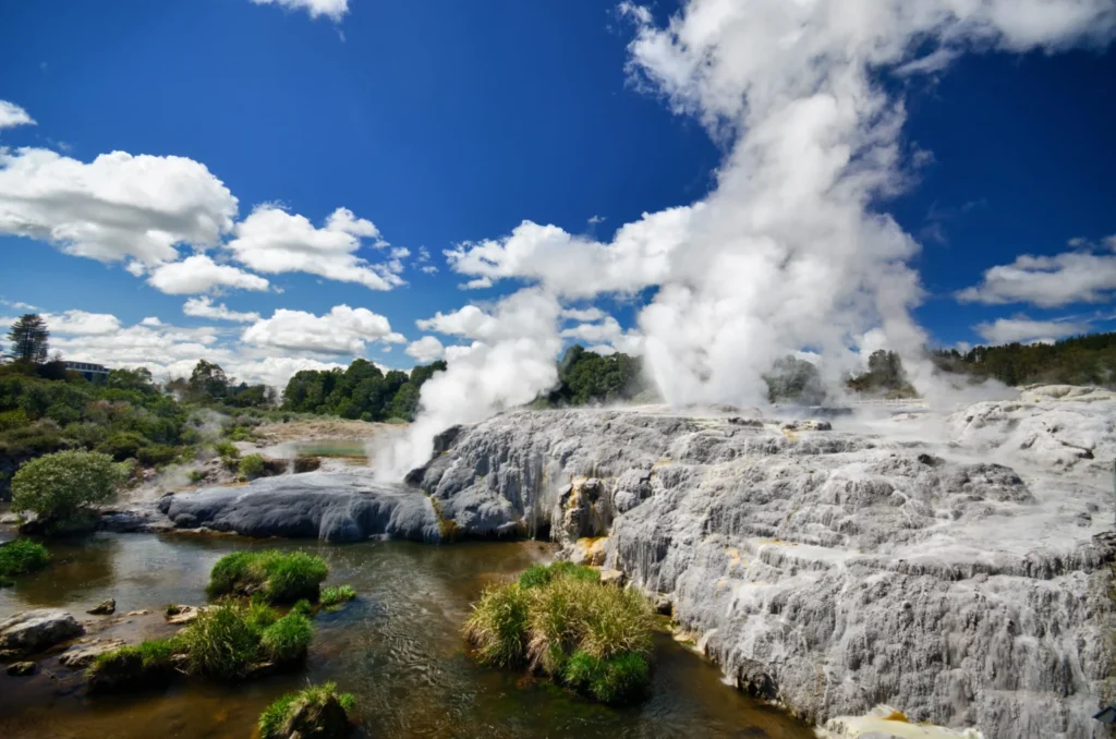 Active geyser with lots of white smoke on grey rocks by a mudpool in Rotorua New Zealand